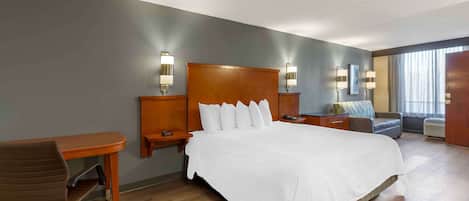 Una habitación de hotel con una cama grande, un escritorio, una silla y dos mesitas de noche con lámparas.