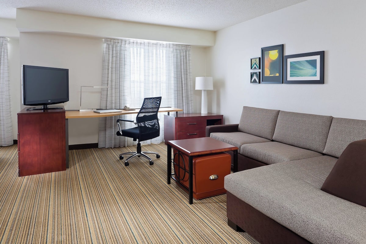 A hotel room with a sofa, a desk with a computer, a TV, and a lamp.
