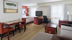 A hotel room with a bed, a desk with a computer, a TV, and a seating area with chairs and a sofa.