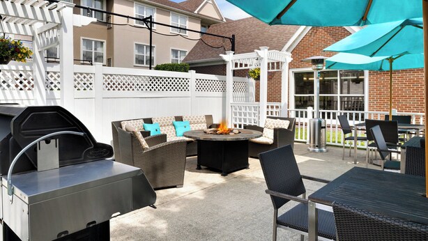 An outdoor patio with a grill, seating area, and umbrellas.