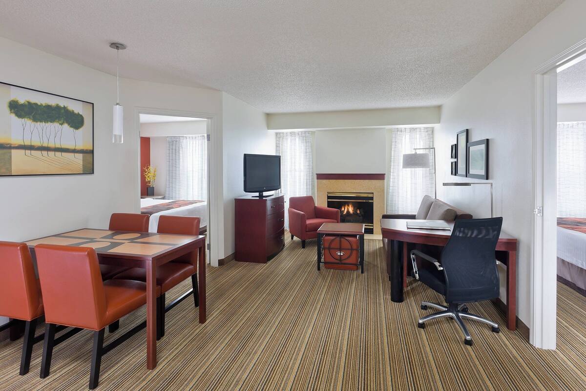 A hotel room with a dining area, a TV, a fireplace, and a bed.