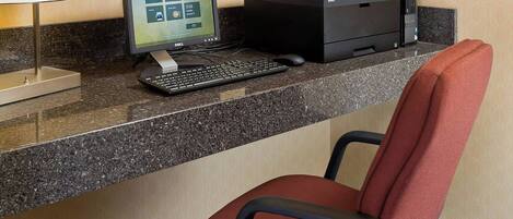 Un mostrador de recepción de hotel con una computadora, una impresora y una silla de oficina roja.