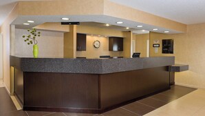 A reception area with a dark wood reception desk, a clock, and a vase with green foliage.