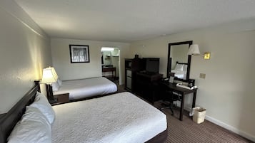 A hotel room with two beds, a desk, a chair, a mirror, and a lamp.