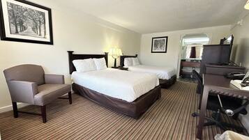 A hotel room with two beds, a chair, a desk, and a TV.
