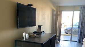 A hotel room with a large flat-screen TV mounted on the wall, a desk with a telephone and a small trash bin, and a view of the parking area through the door. - Days Inn by Wyndham Okmulgee (Okmulgee)