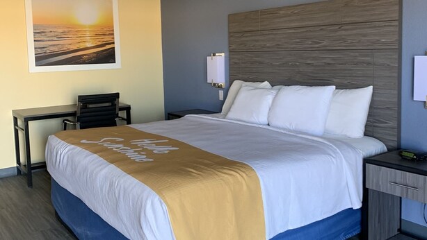 A hotel room with a bed, a desk, a chair, a nightstand, and a wall-mounted lamp. - Days Inn by Wyndham Okmulgee (Okmulgee)