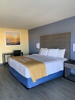 Habitación de hotel con cama, escritorio, silla, mesita de noche y lámpara de pared.