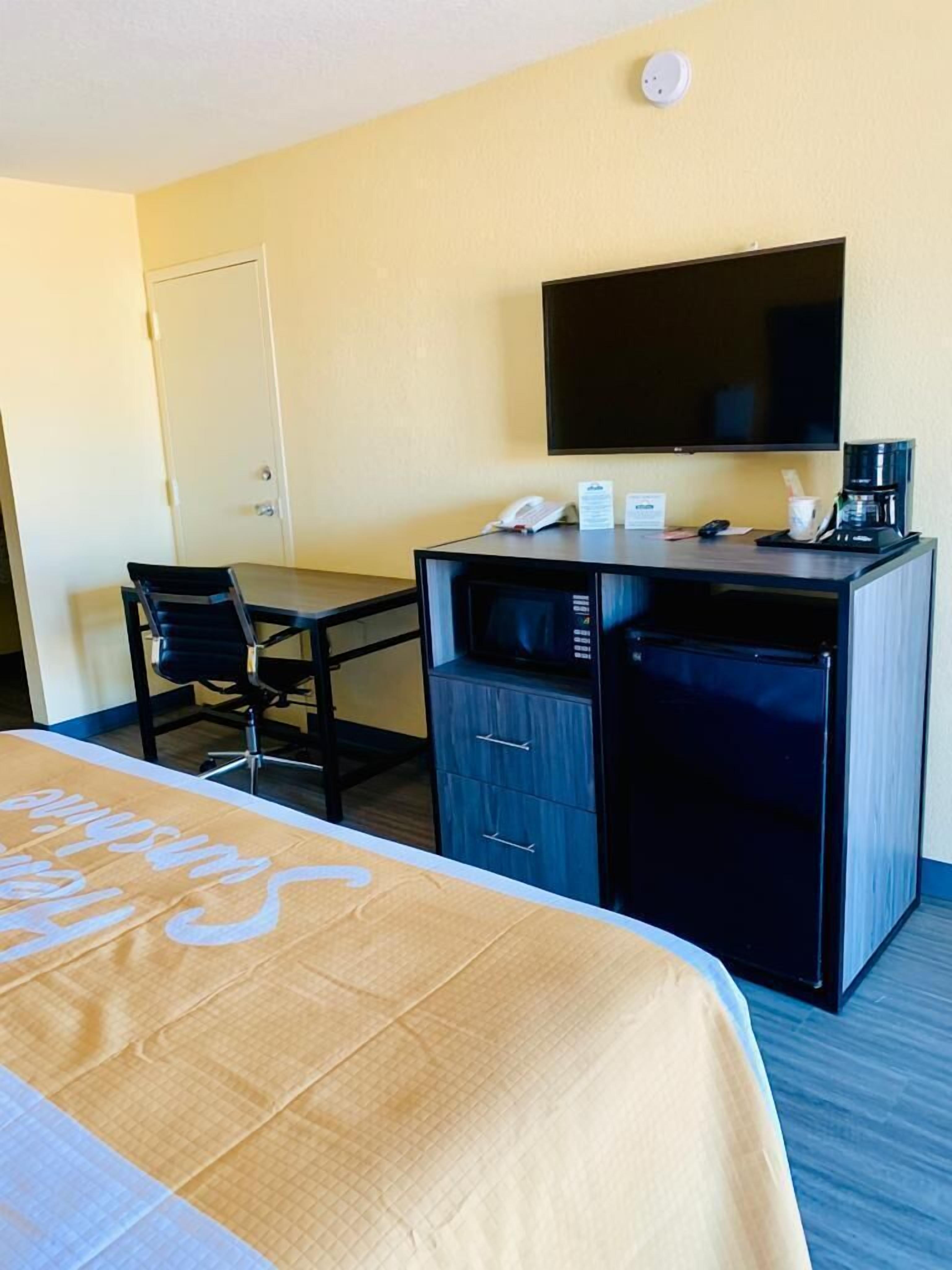 A hotel room with a bed, a desk, a chair, a television, and a coffee maker.