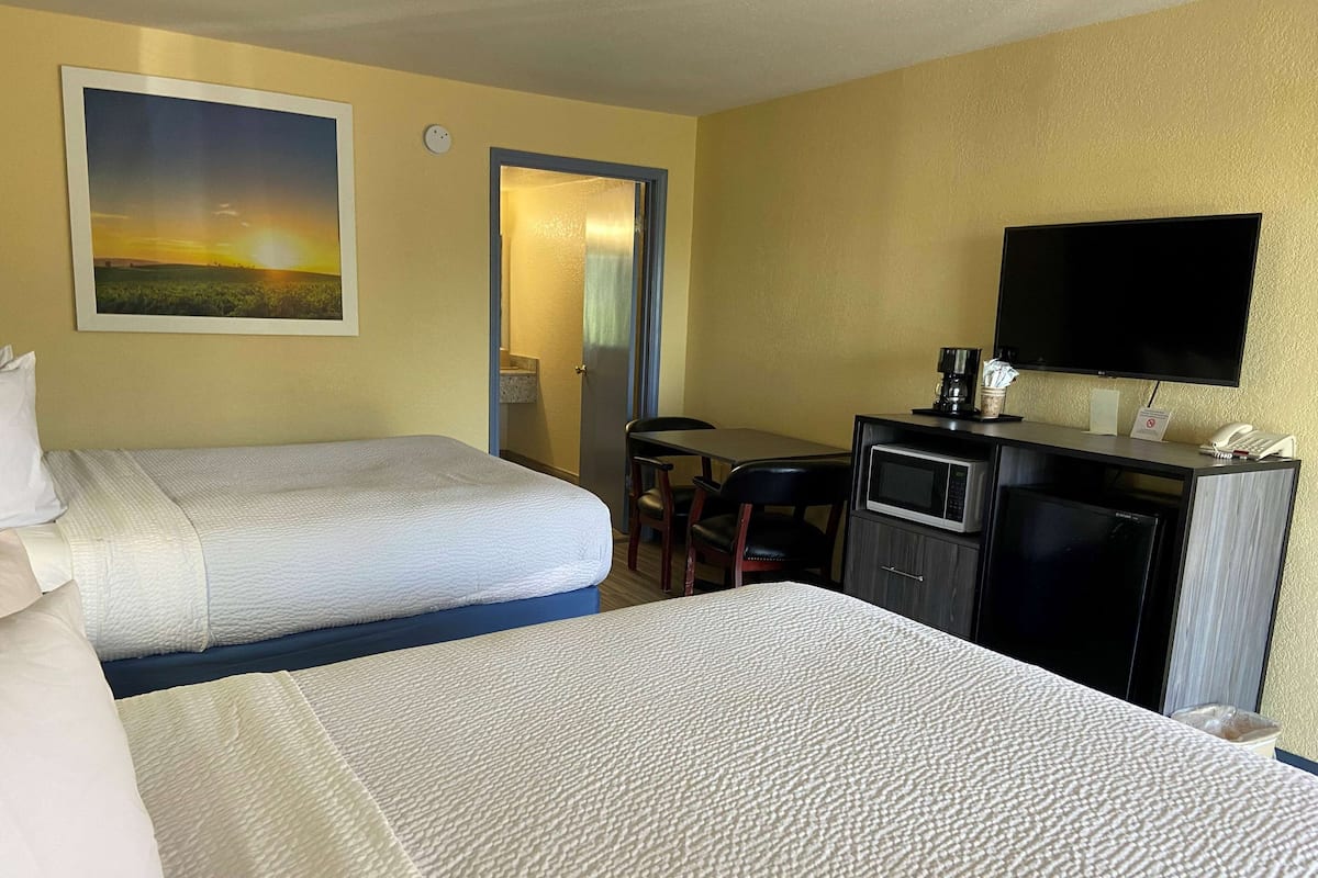 A hotel room with two beds, a desk with a computer, a television, and a painting of a sunset.