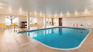 Una piscina interior con agua cristalina y azul, rodeada de sillas amarillas y un suelo de baldosas.