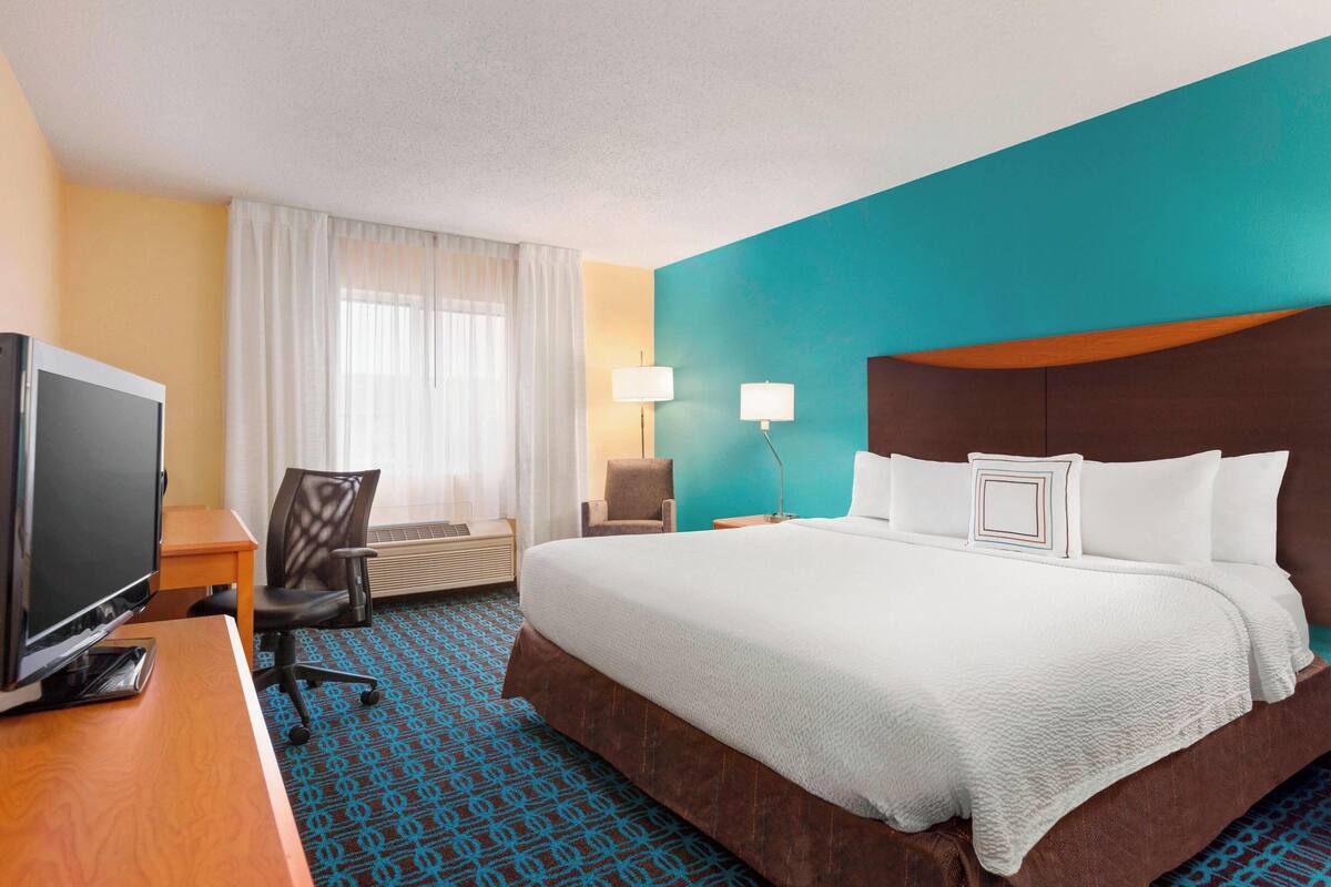 A hotel room with a large bed, a desk with a TV, a chair, and a window with curtains.