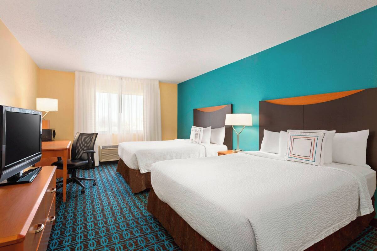 A hotel room with two beds, a TV, a desk, and a chair.