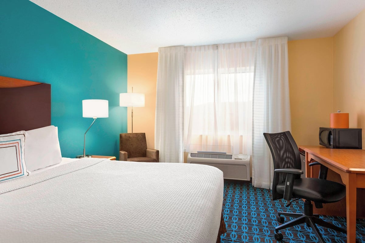 Une chambre d’hôtel équipée d’un lit, d’un bureau, d’une chaise, d’une télévision et d’une fenêtre avec des rideaux.