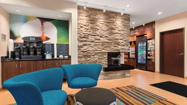 Un hall de hotel con pared de piedra, una estación de café, un refrigerador y sillas azules.