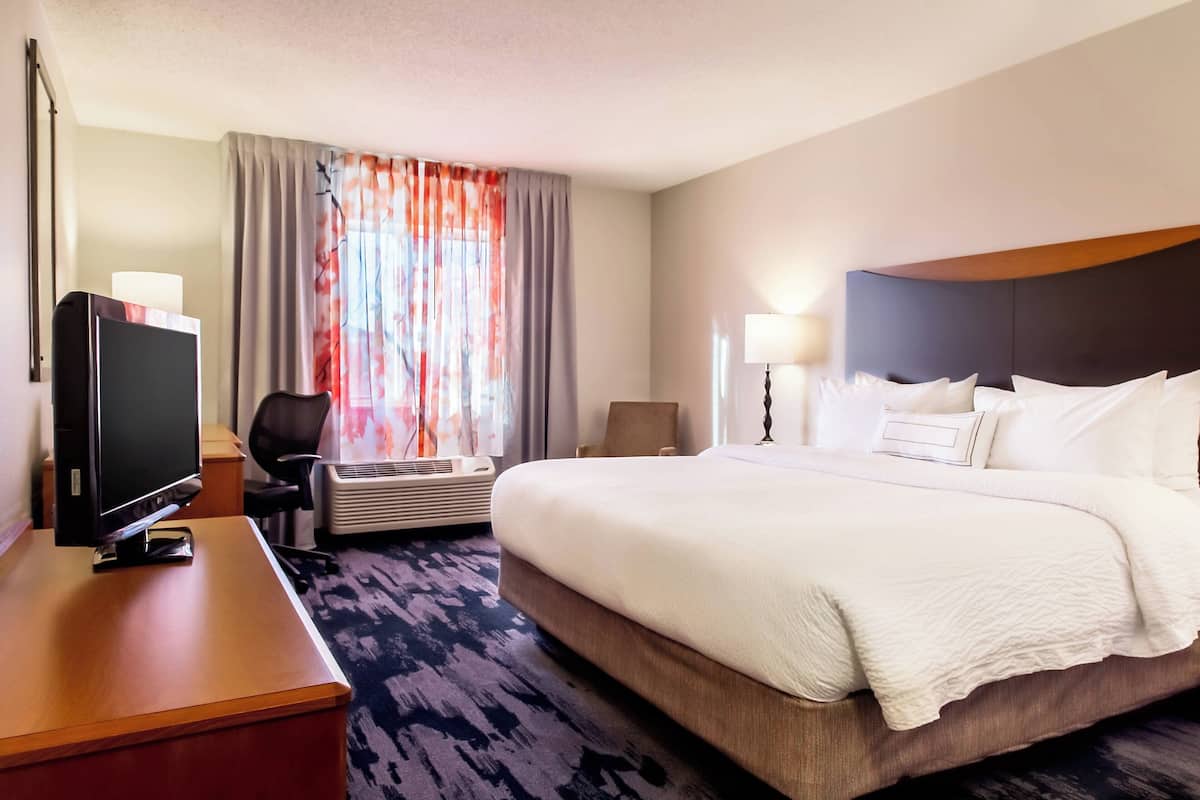 Une chambre d’hôtel avec un grand lit, un bureau doté d’un téléviseur à écran plat, une chaise et une fenêtre avec des rideaux.