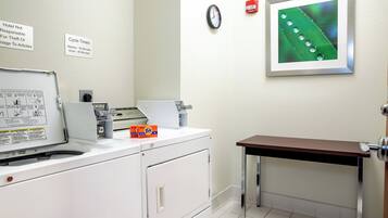 A laundry area with a washing machine, a dryer, and a table. There are signs on the wall indicating cycle times and a notice about theft.
