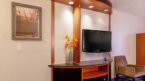 Una sala de estar moderna con un mueble curvo para entretenimiento, un televisor de pantalla plana, un florero con flores y un sillón cómodo.
