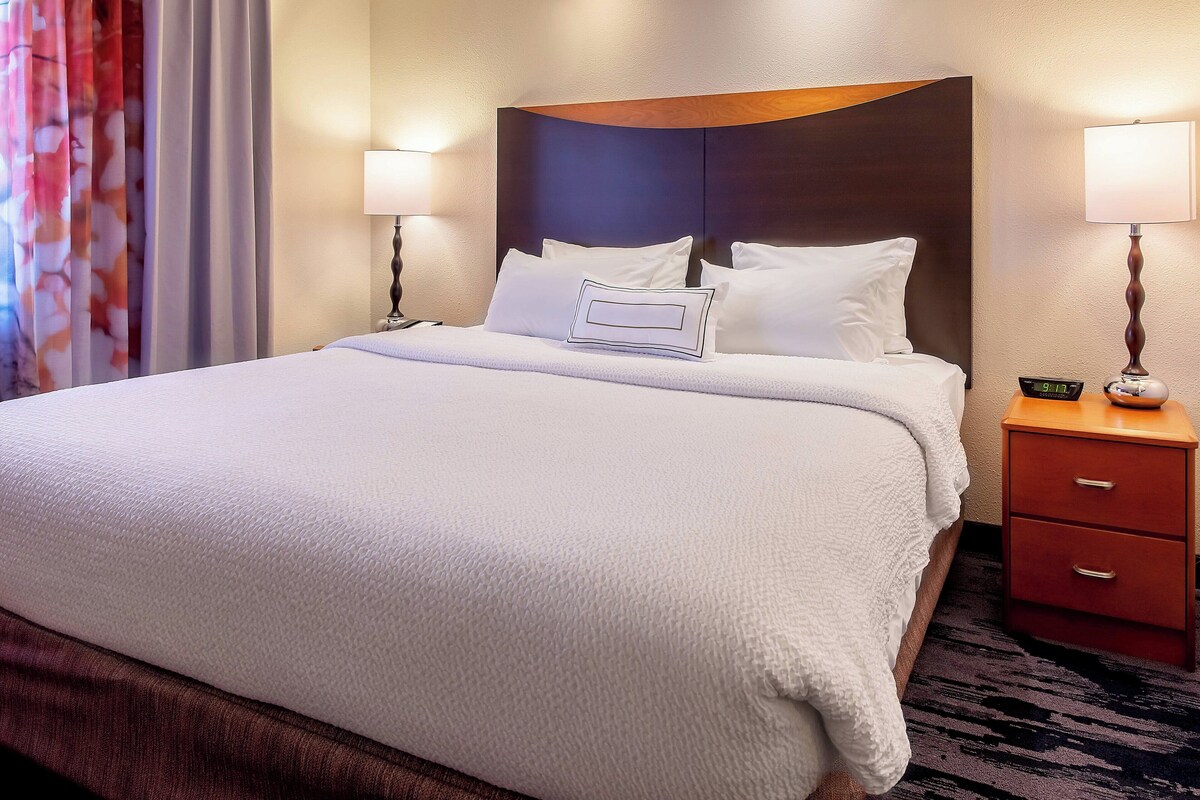 Habitación de hotel con una cama grande, dos mesitas de noche y un reloj de pared.
