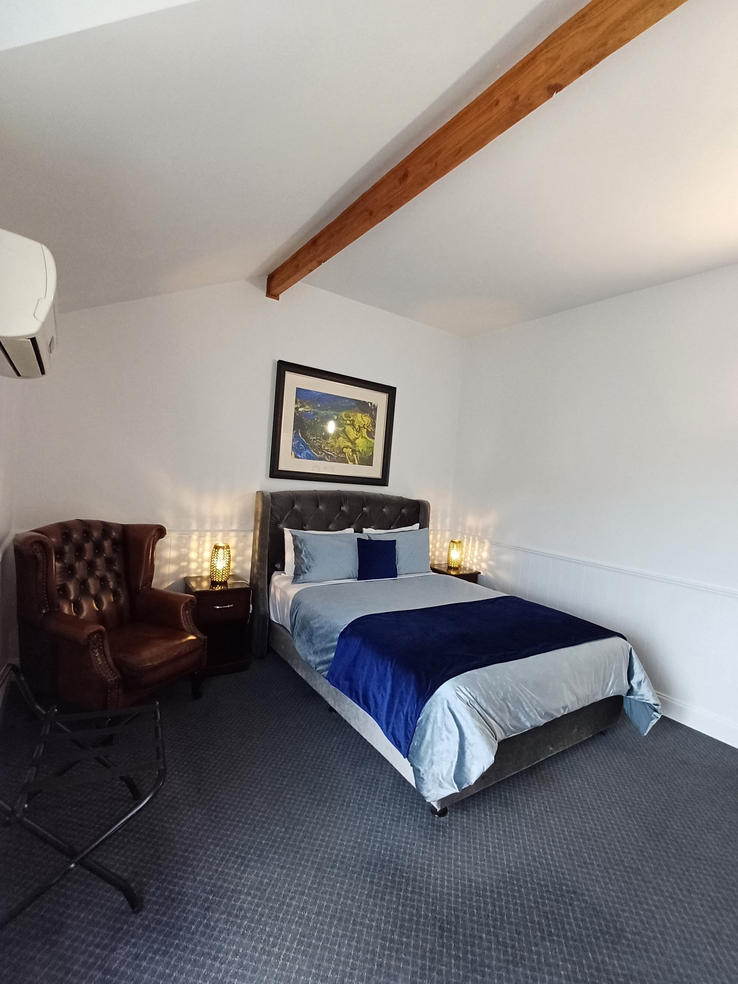 Une chambre à coucher avec un lit, une chaise, une table de chevet avec une lampe et un tableau encadré au mur.