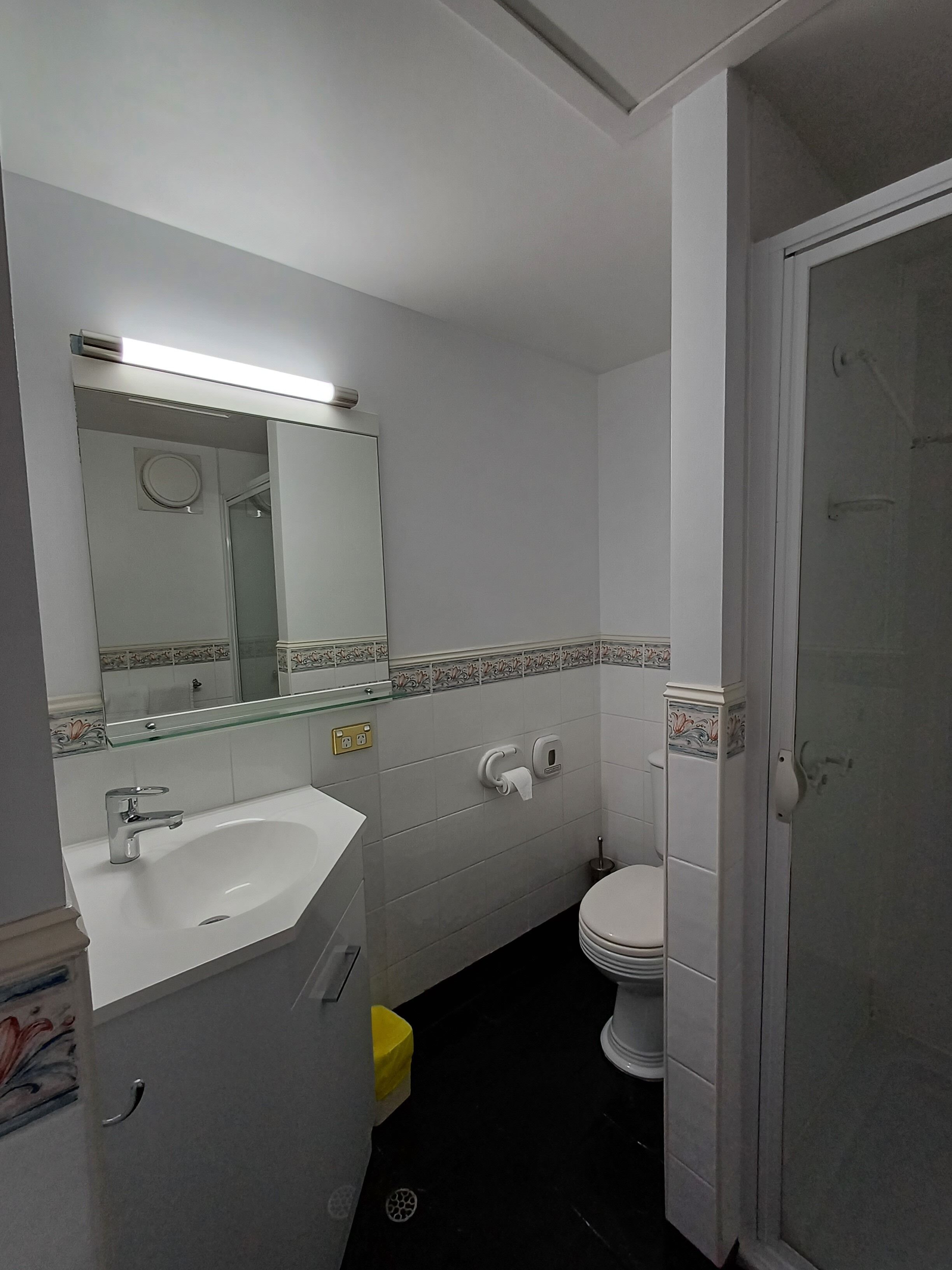 A bathroom with a white sink, mirror, toilet, and a glass shower enclosure.