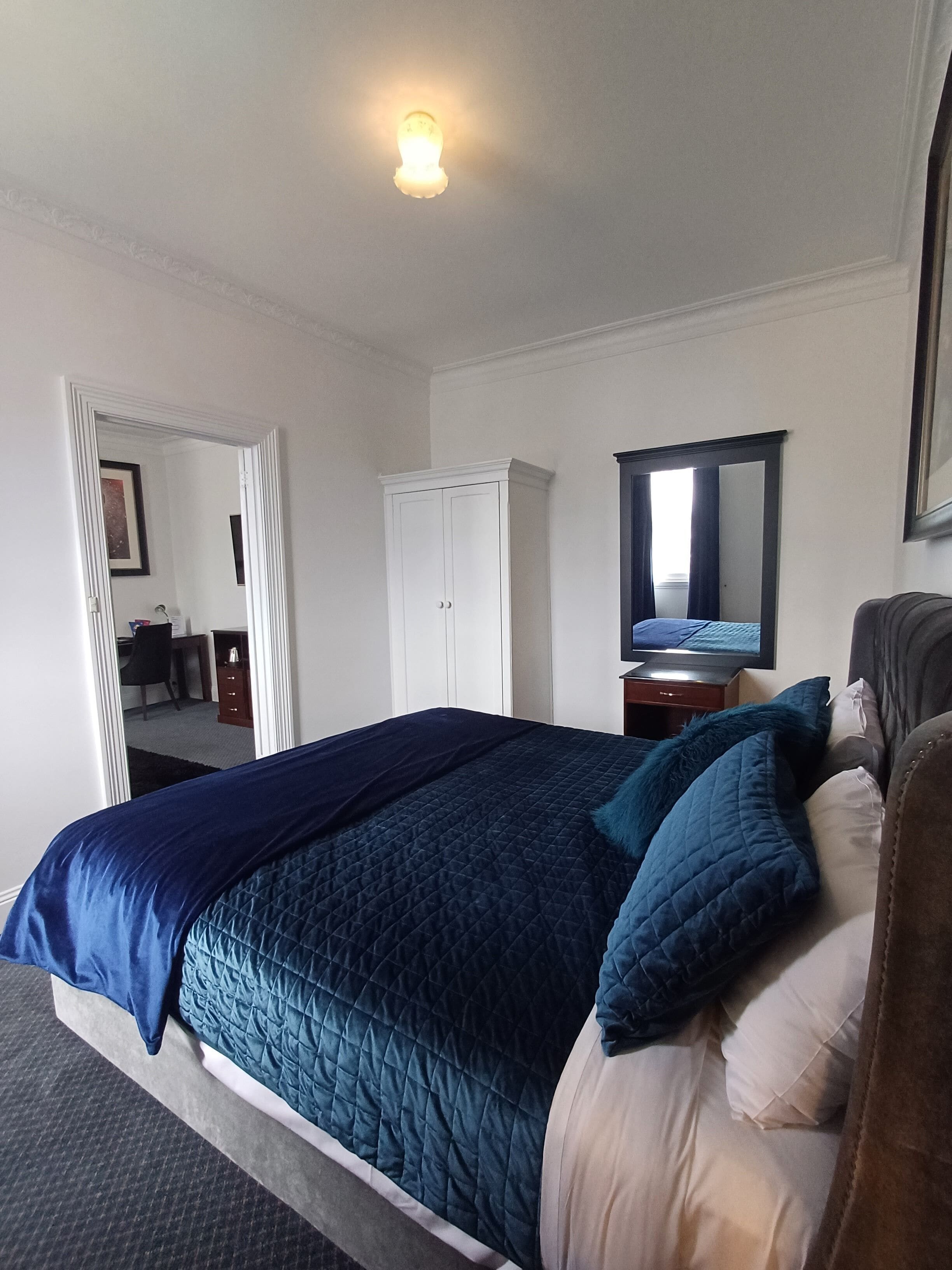 A neatly arranged bedroom with a bed, a wardrobe, a mirror, and a desk.