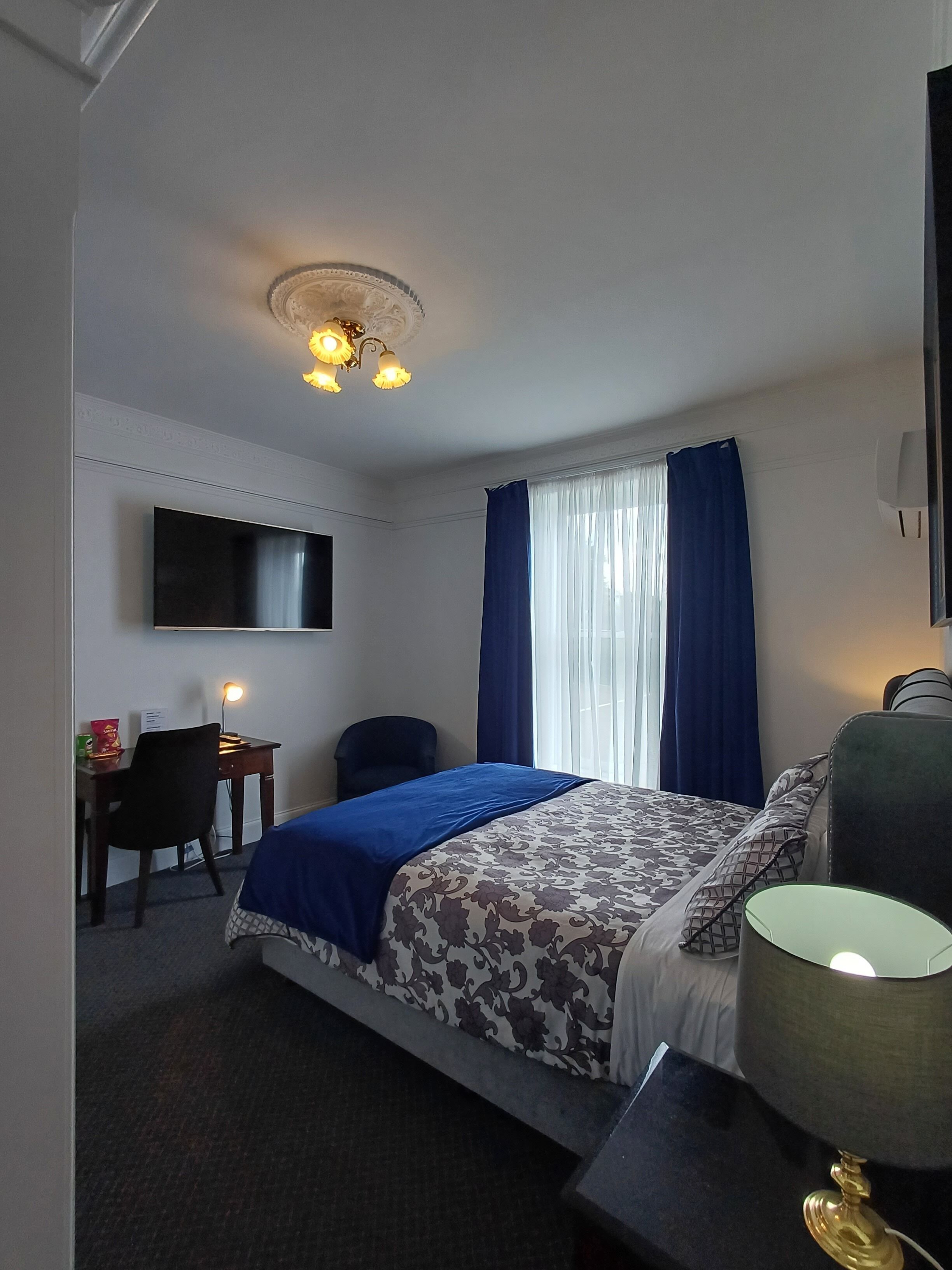 Una habitación de hotel con cama, escritorio, silla, televisor y lámpara.
