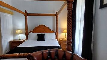 Ein Bett mit Baldachin, ein Holzkopfstück, ein Stuhl mit gepolstertem Rücken und zwei Nachttische mit Lampen.