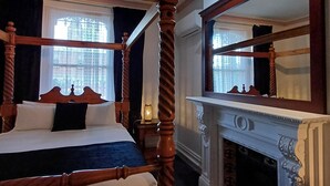 Una cama con dosel, un espejo encima, una chimenea y una ventana con cortinas.