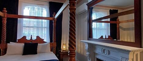 Een hemelbed met een spiegel erboven, een open haard en een raam met gordijnen.