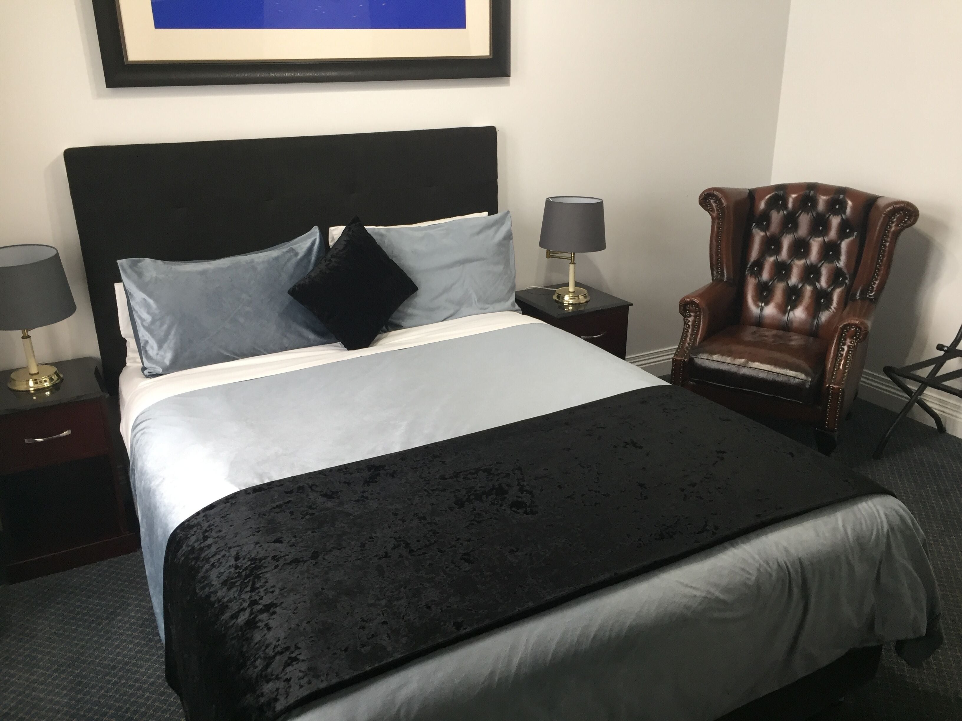 A neatly made bed with a black headboard, two bedside tables with lamps, and a leather armchair.