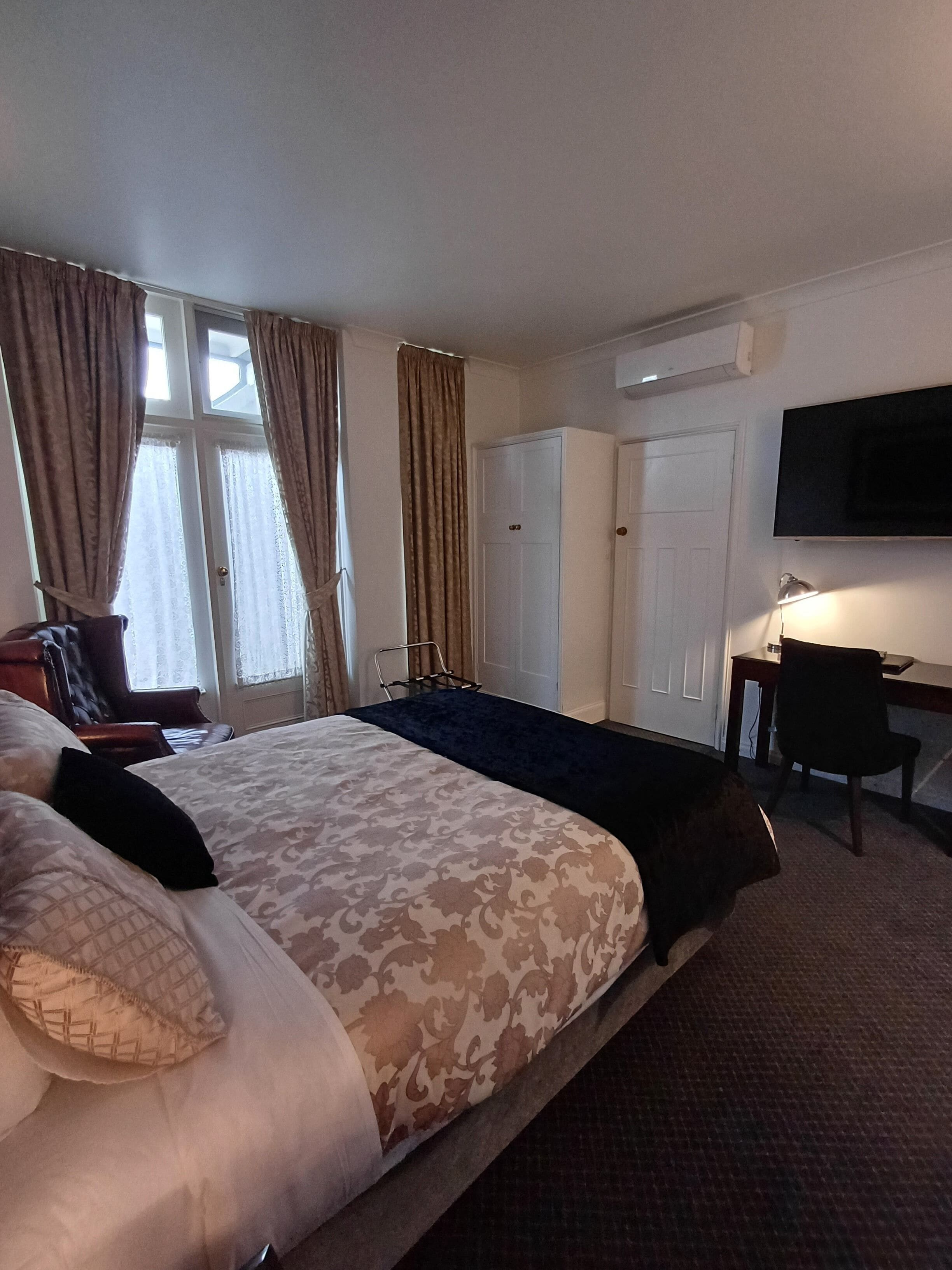 A hotel room with a large bed, a desk, a chair, and a TV.