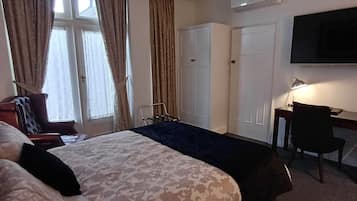 A hotel room with a large bed, a desk, a chair, and a TV.
