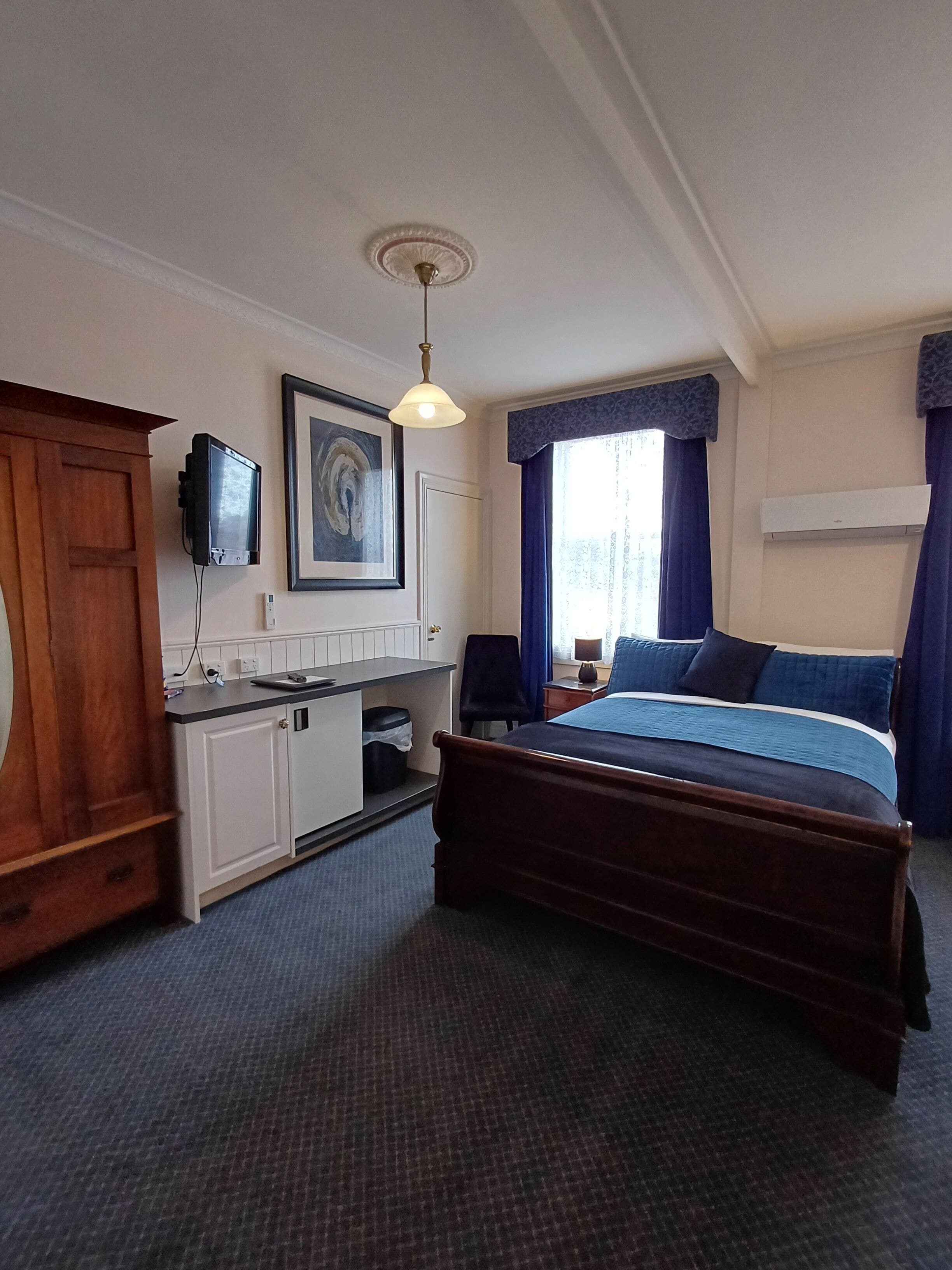 A hotel room with a bed, a desk, a television, and a window with curtains.
