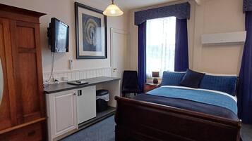 A hotel room with a bed, a desk, a television, and a window with curtains.