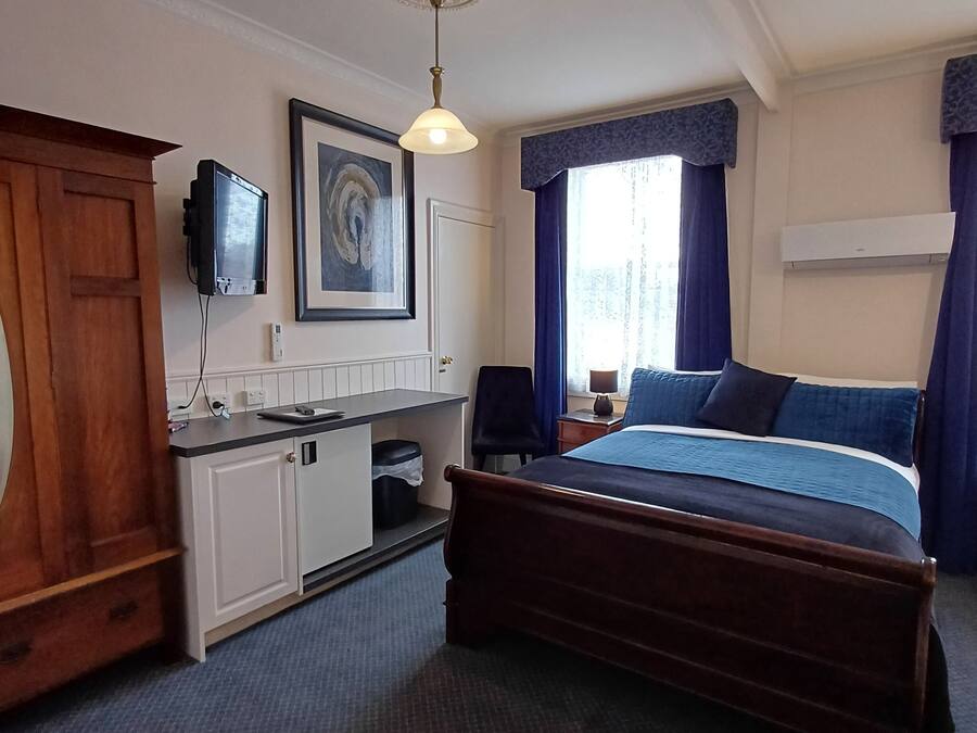 A hotel room with a bed, a desk, a television, and a window with curtains.