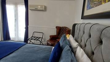 A bedroom with a large bed, a chair, a painting, and an air conditioning unit.