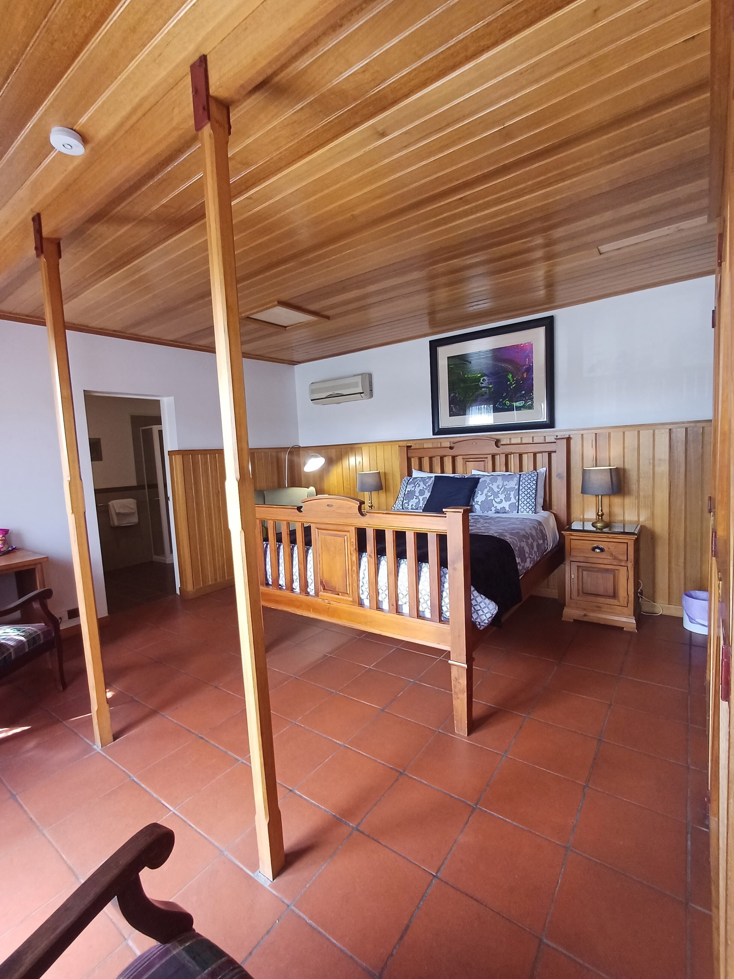 Quarto com cama de madeira, mesa de cabeceira, luminária e quadro na parede.