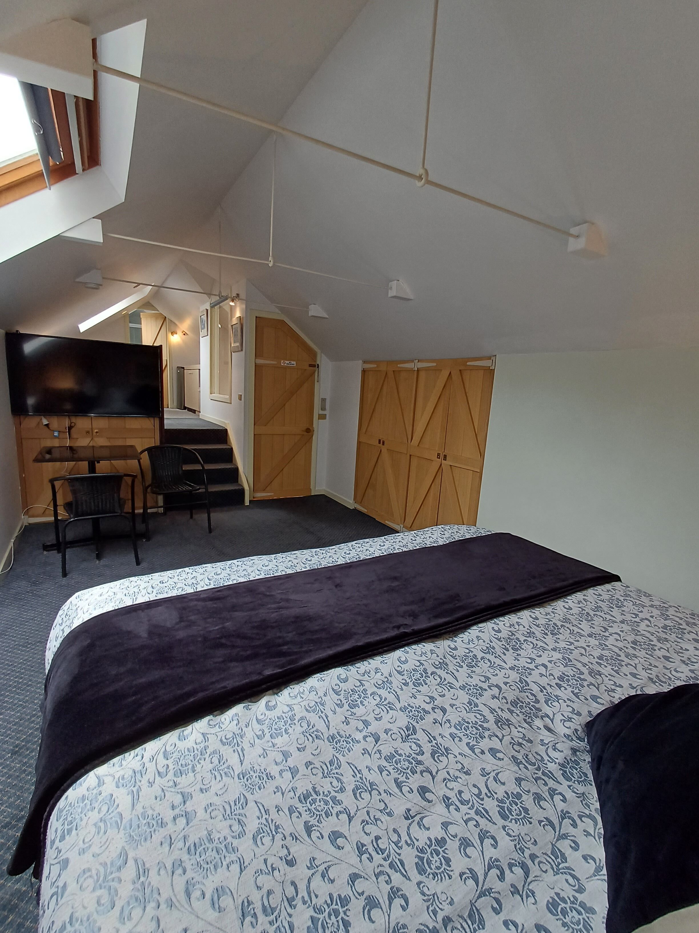 A bedroom with a large bed, a desk, a chair, a television, and a wardrobe.