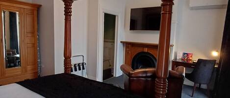 Una cama con dosel, un tablero de cama oscuro, un armario de madera, un televisor montado en la pared y una chimenea.