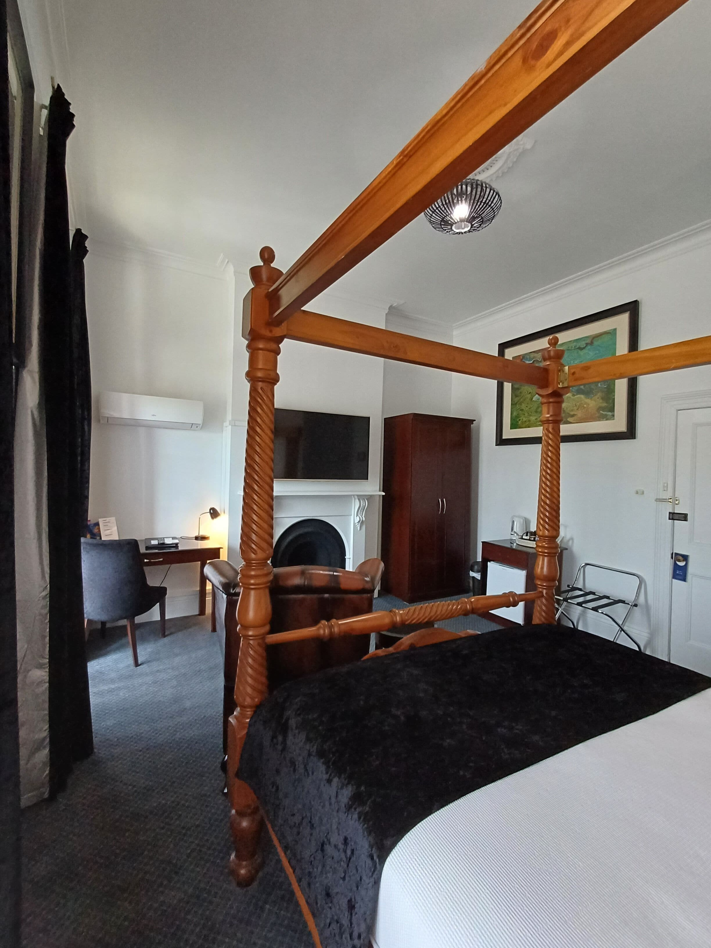 Una cama con dosel, un tablero oscuro, un escritorio con una silla, un televisor, un armario y un cuadro en la pared.