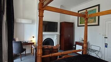 Una cama con dosel, un tablero oscuro, un escritorio con una silla, un televisor, un armario y un cuadro en la pared.