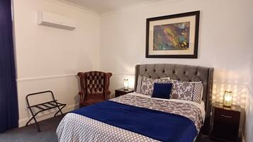 A neatly arranged hotel room with a bed, a chair, a nightstand, and a wall-mounted air conditioner.