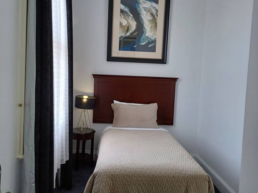 A hotel room with a single bed, a headboard, a framed abstract painting, a bedside lamp, and a window with curtains.