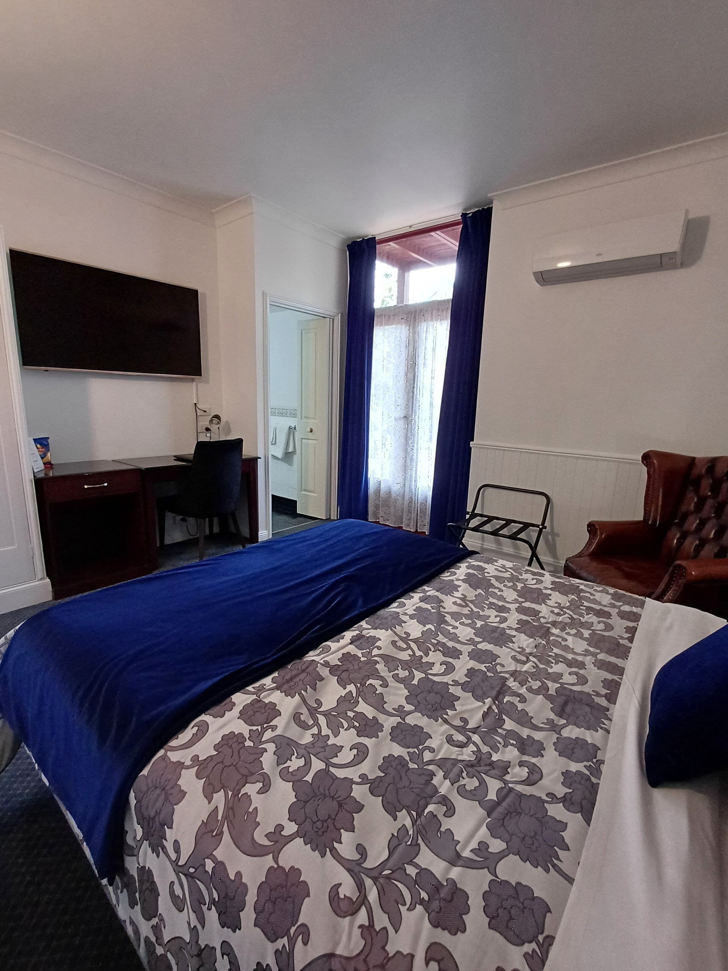 A hotel room with a bed, a desk, a chair, and a TV mounted on the wall.
