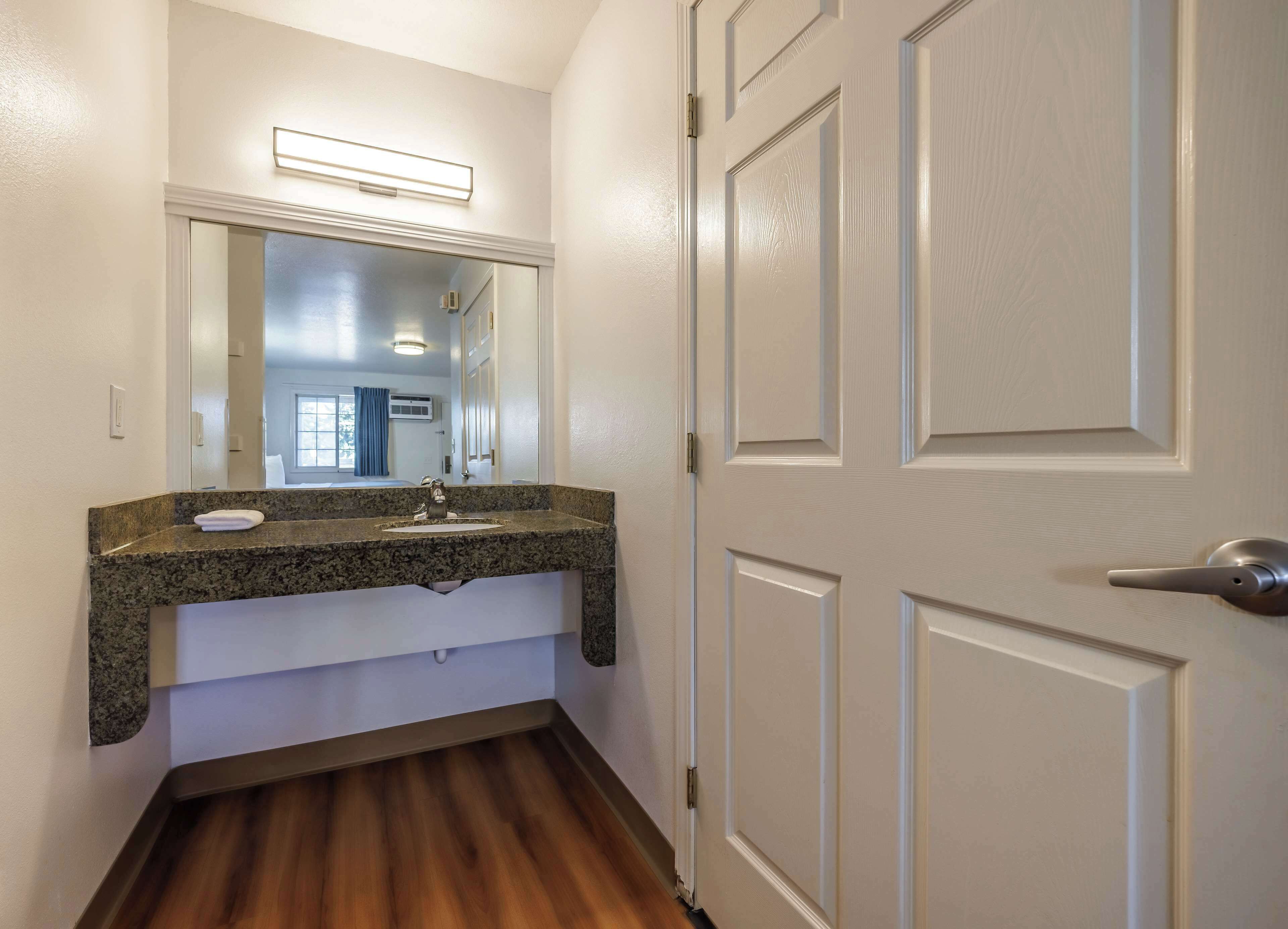 A bathroom with a granite countertop sink, a mirror above it, and a wooden floor.