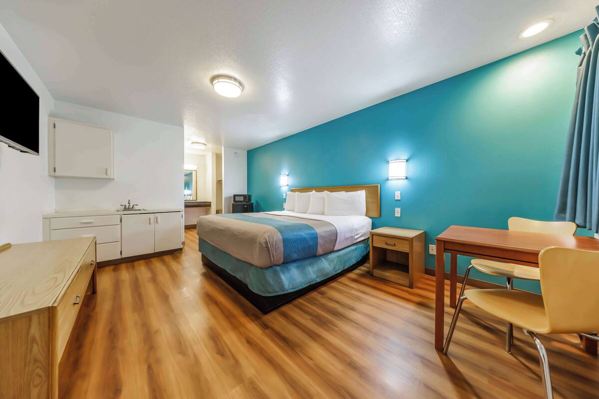 Quarto de hotel com cama, escrivaninha, cadeira, mesa e televisão.