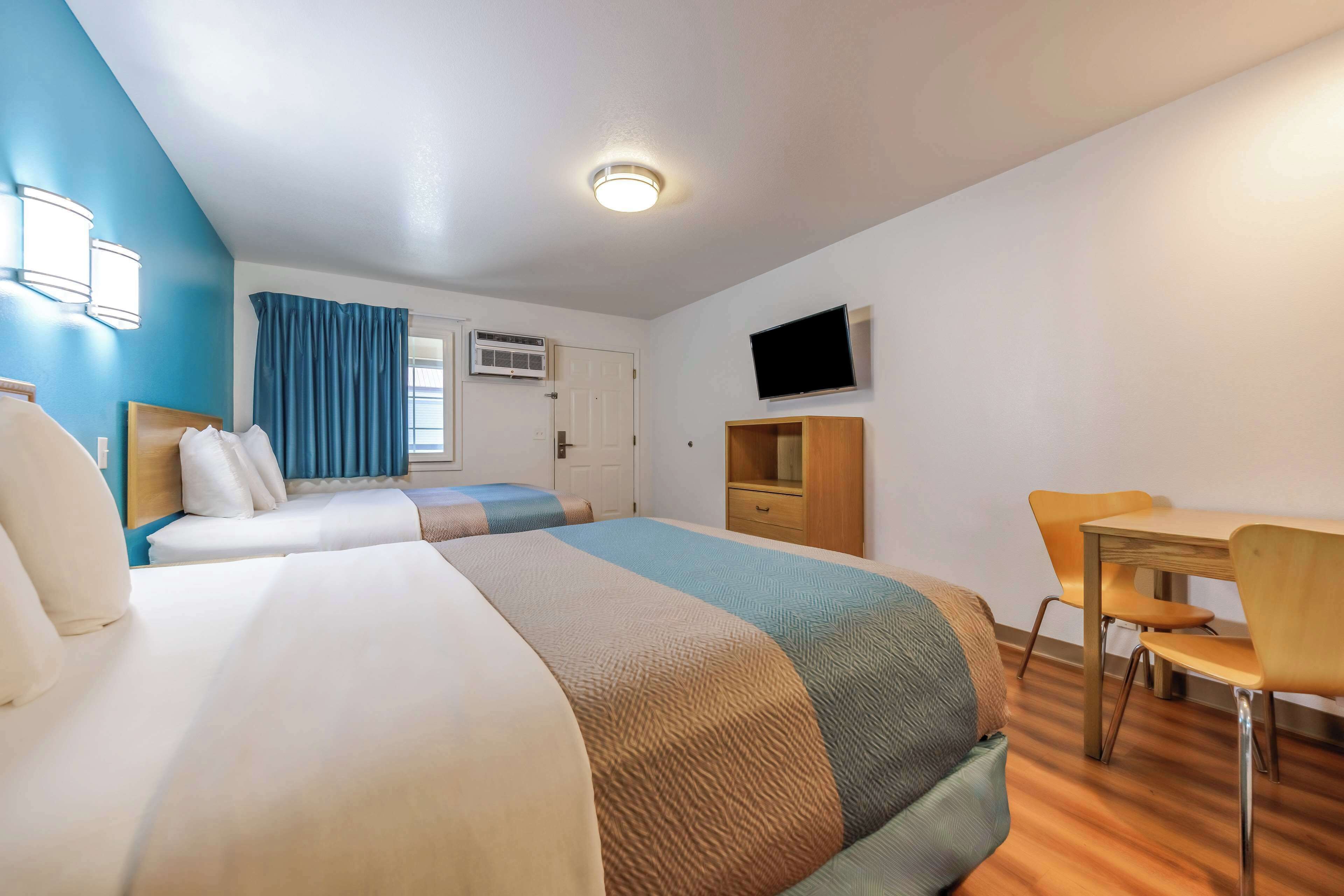 A hotel room with two beds, a desk, a chair, a TV, and a window with curtains.