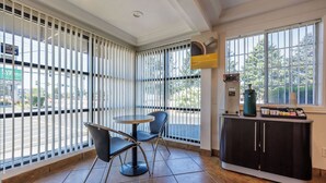 A room with a large window, a round table with chairs, a cabinet with a coffee machine, and a sign on the window. - Motel 6 Canby, OR (Canby)