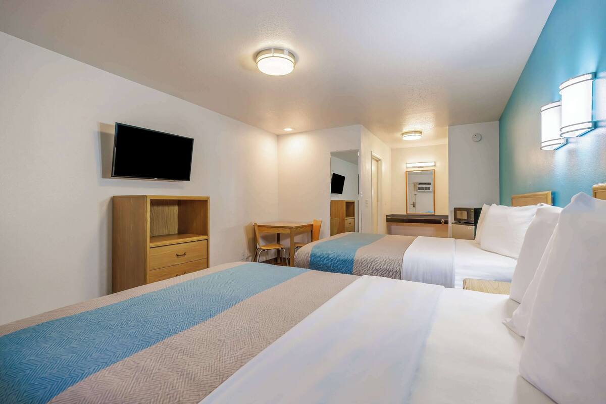 Quarto de hotel com duas camas, uma escrivaninha, uma cadeira, uma televisão e um espelho.